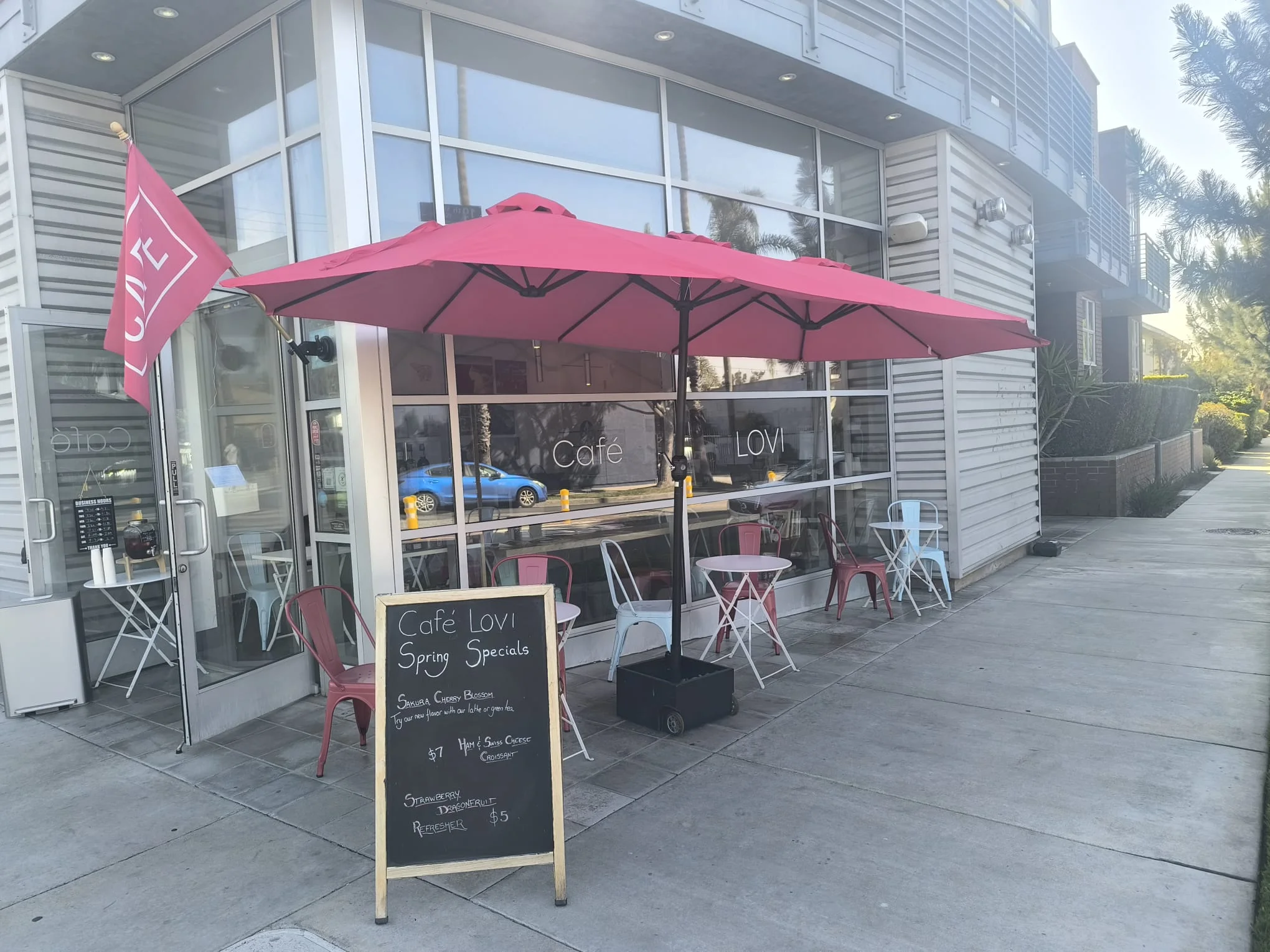 Charming café exterior with pink umbrellas and spring specials sign