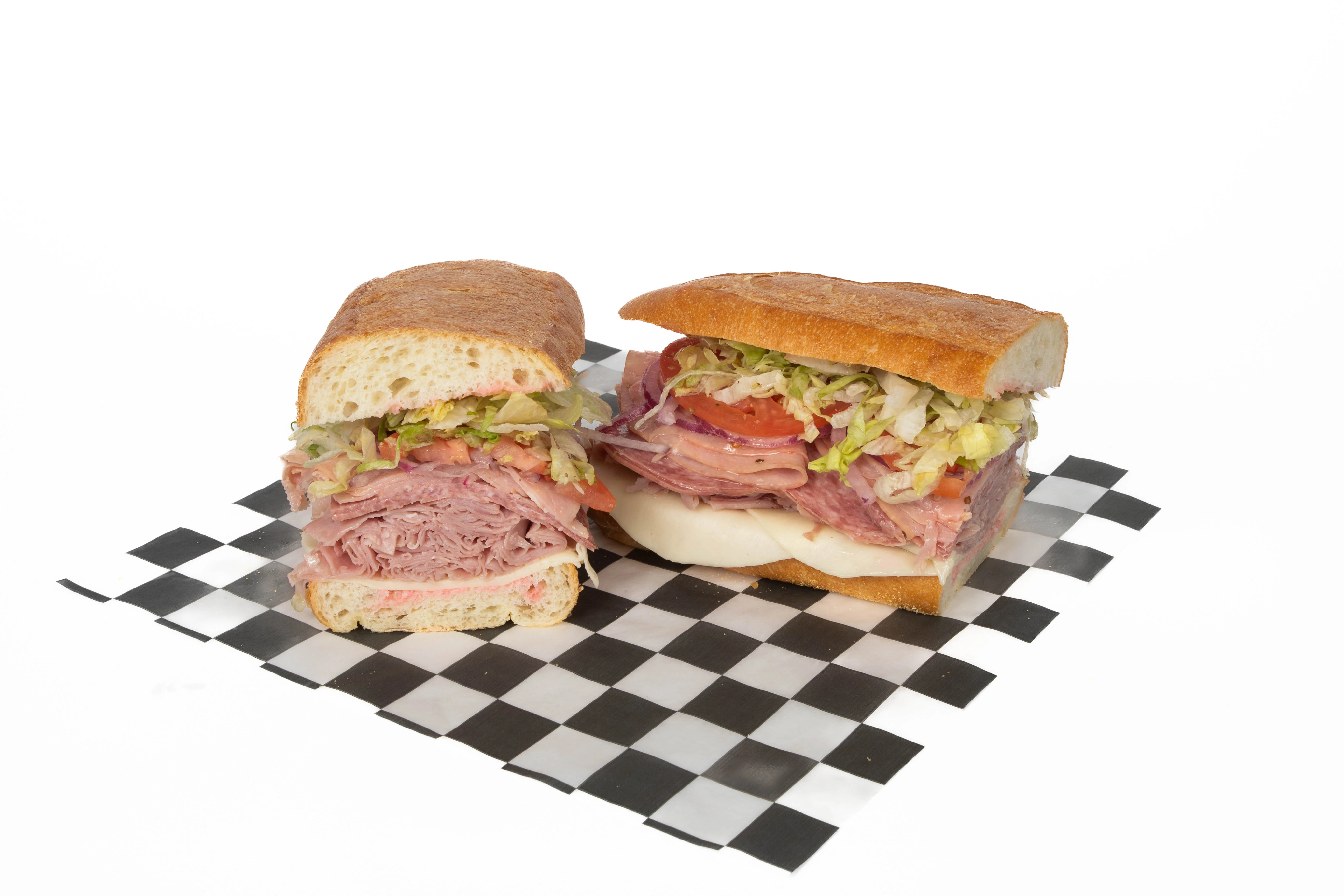 A sandwich filled with layers of deli meats, lettuce, and tomato, served on a checkered board.