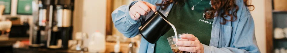 Barista pouring milk into iced coffee drink