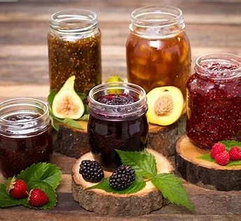 A jar of colorful jam with fruit pieces on a wooden table.