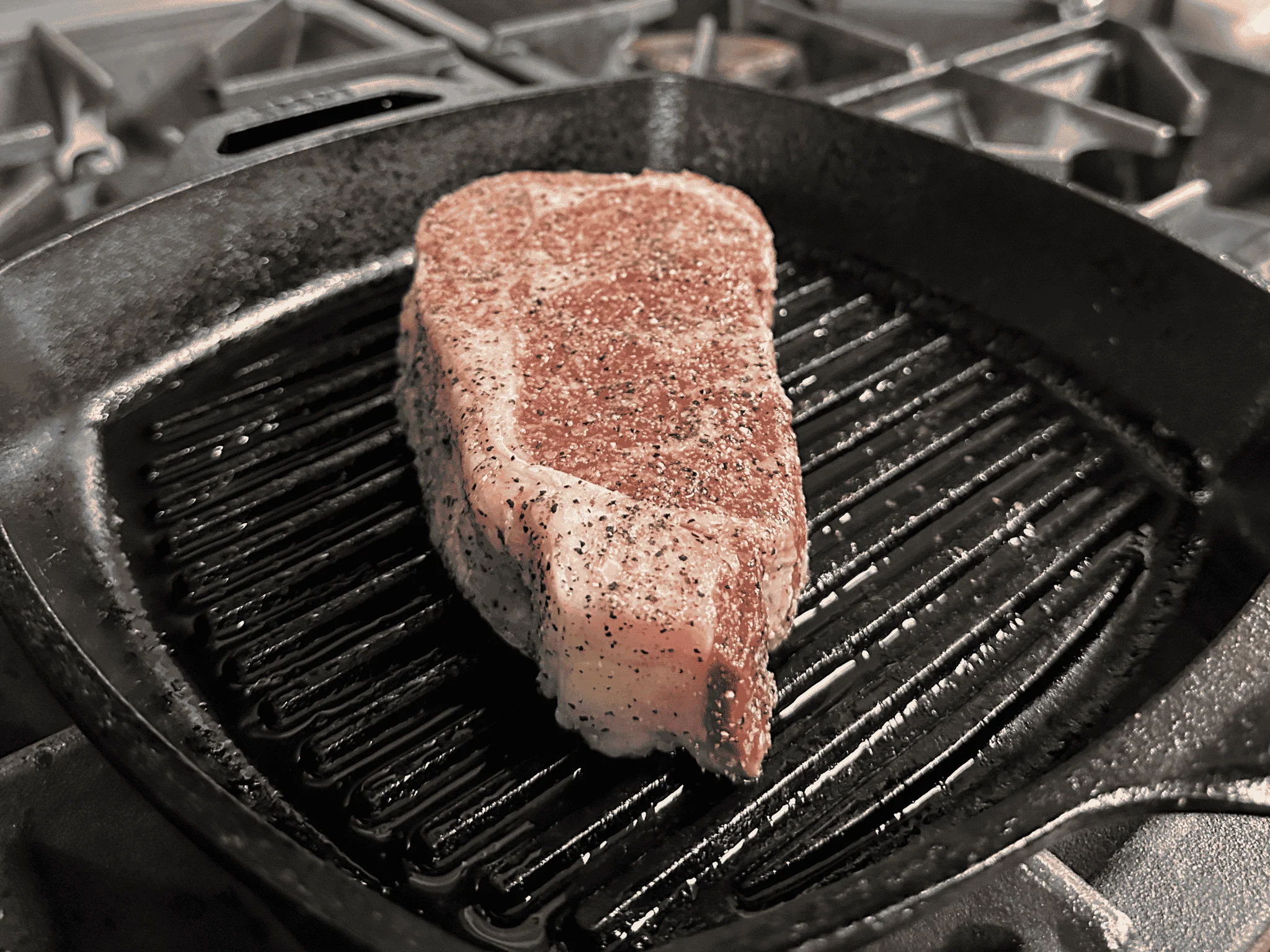 A seasoned steak cooking on a grill pan.