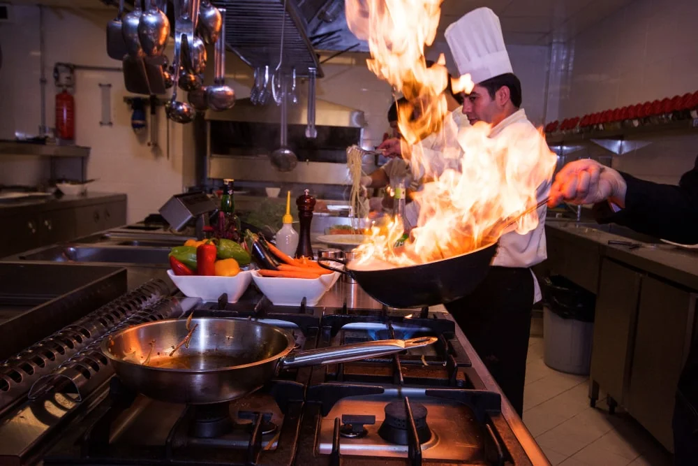 Chef preparing a flaming wok stir-fry in a restaurant kitchen