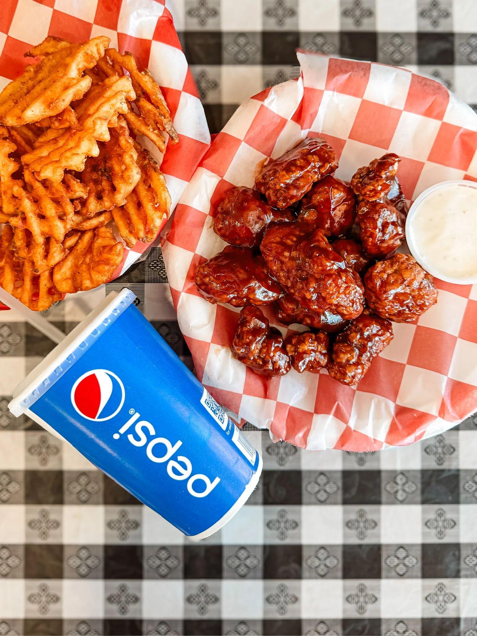 Crispy buffalo wings with waffle fries and a soda