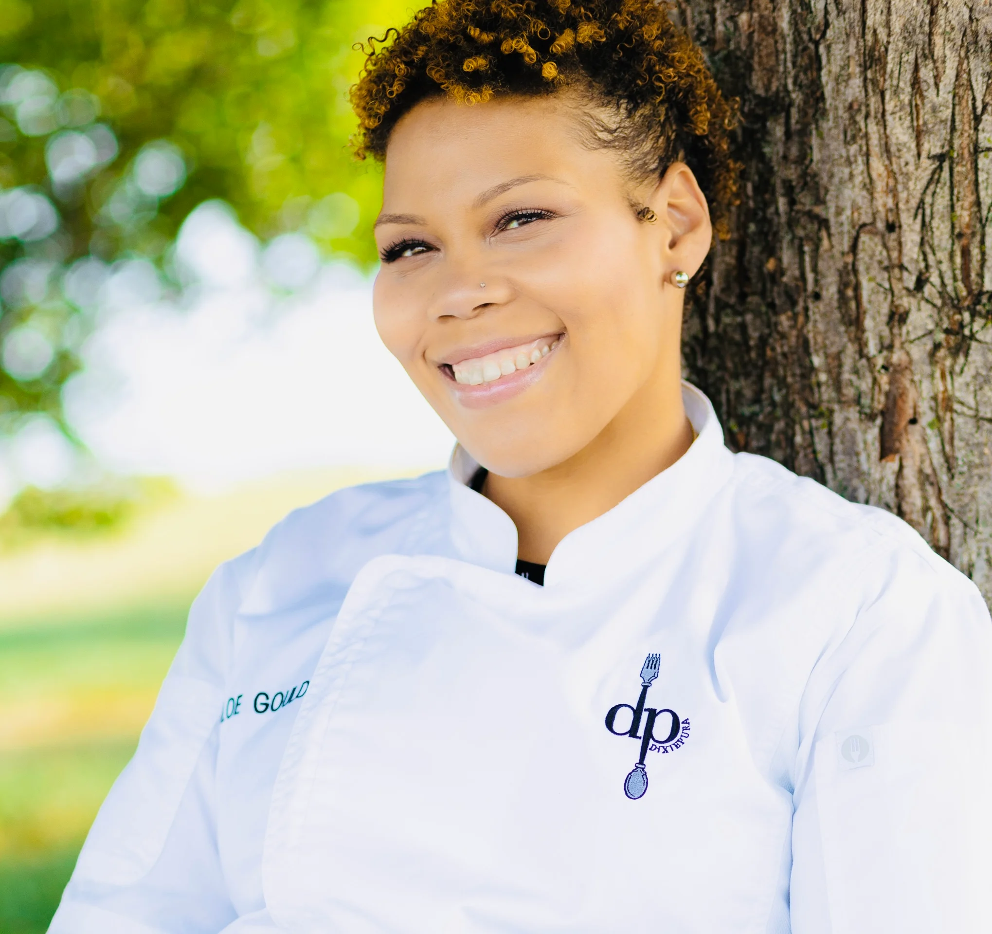 Chef smiling outdoors in a professional kitchen uniform