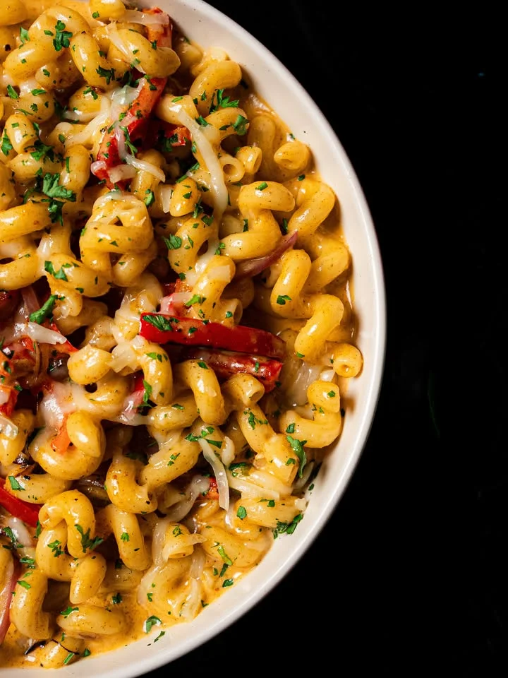 A bowl of pasta featuring curly macaroni mixed with flavorful sauce, peppers, and topped with parsley.
