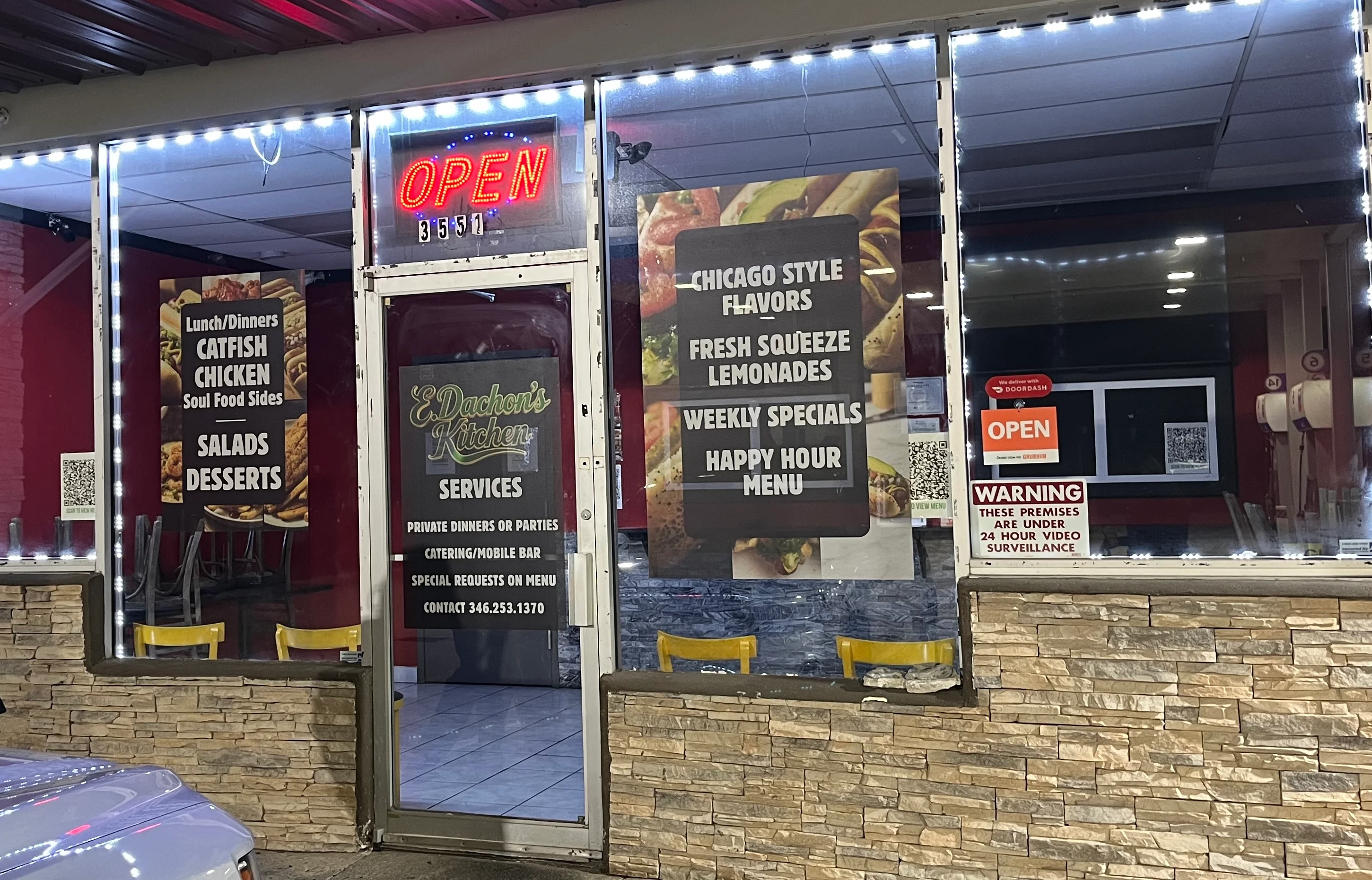 A restaurant facade featuring a brightly lit 'OPEN' sign. The entrance displays menus for catfish, chicken, and soul food, alongside an inviting atmosphere.
