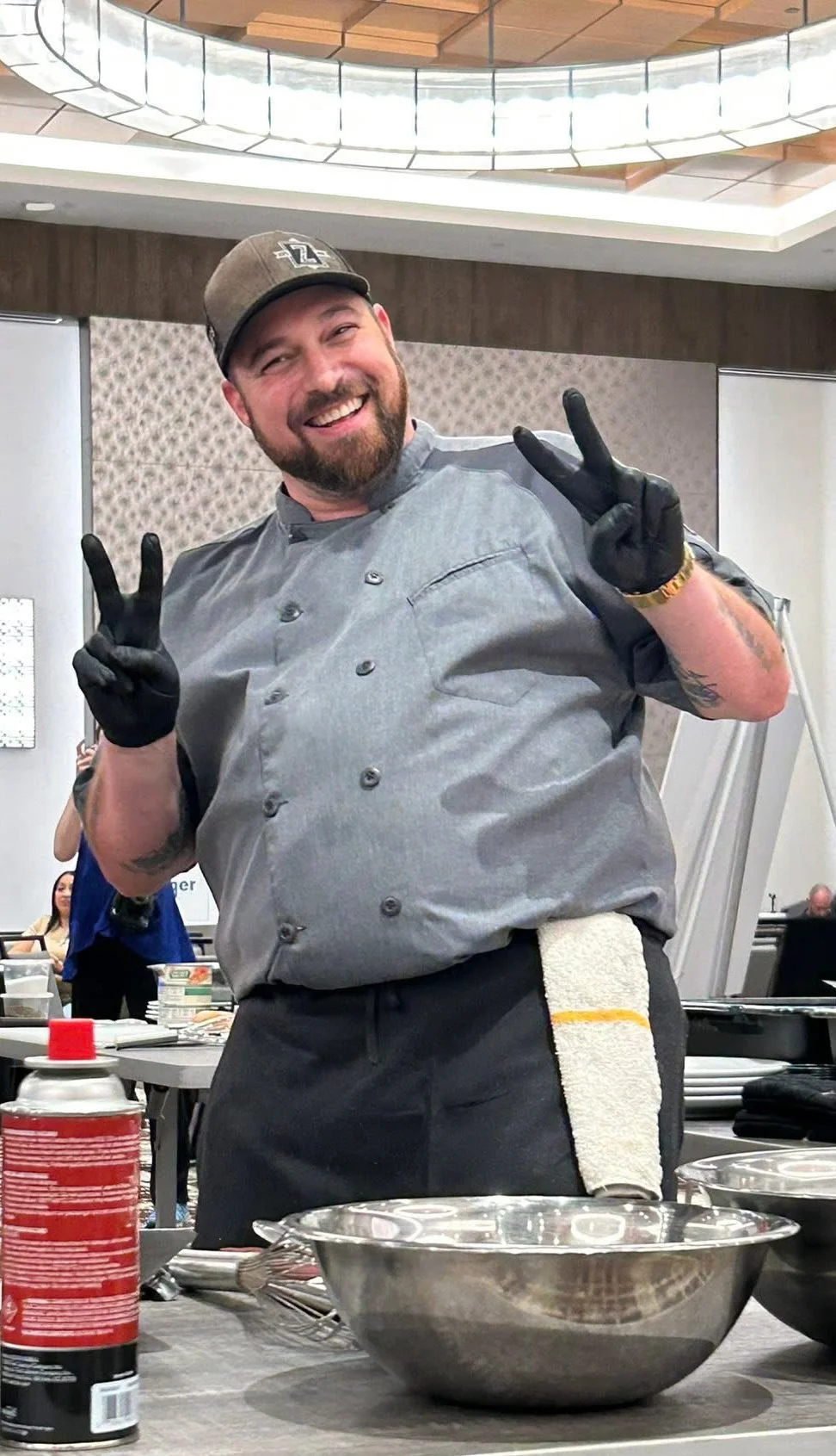 Chef smiling and posing with peace signs in a kitchen setting