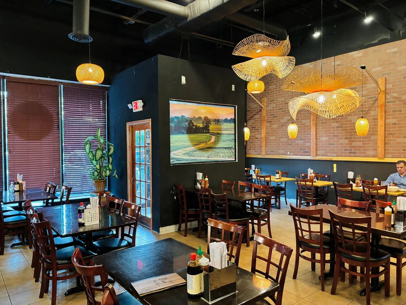 An indoor dining area with dark walls, wooden tables, and modern light fixtures, creating a cozy atmosphere for diners.