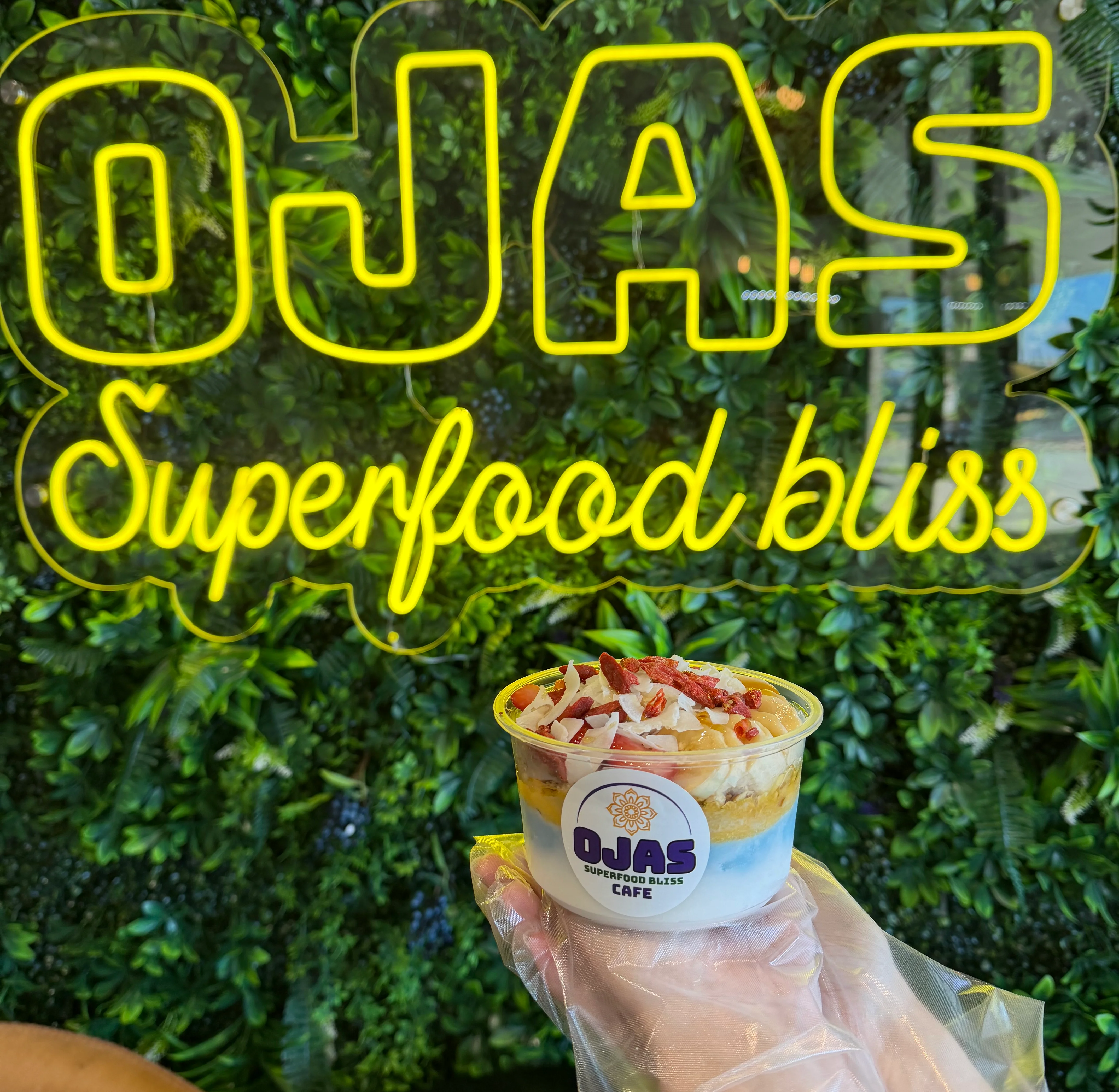 Ojas Café superfood drink in front of neon sign