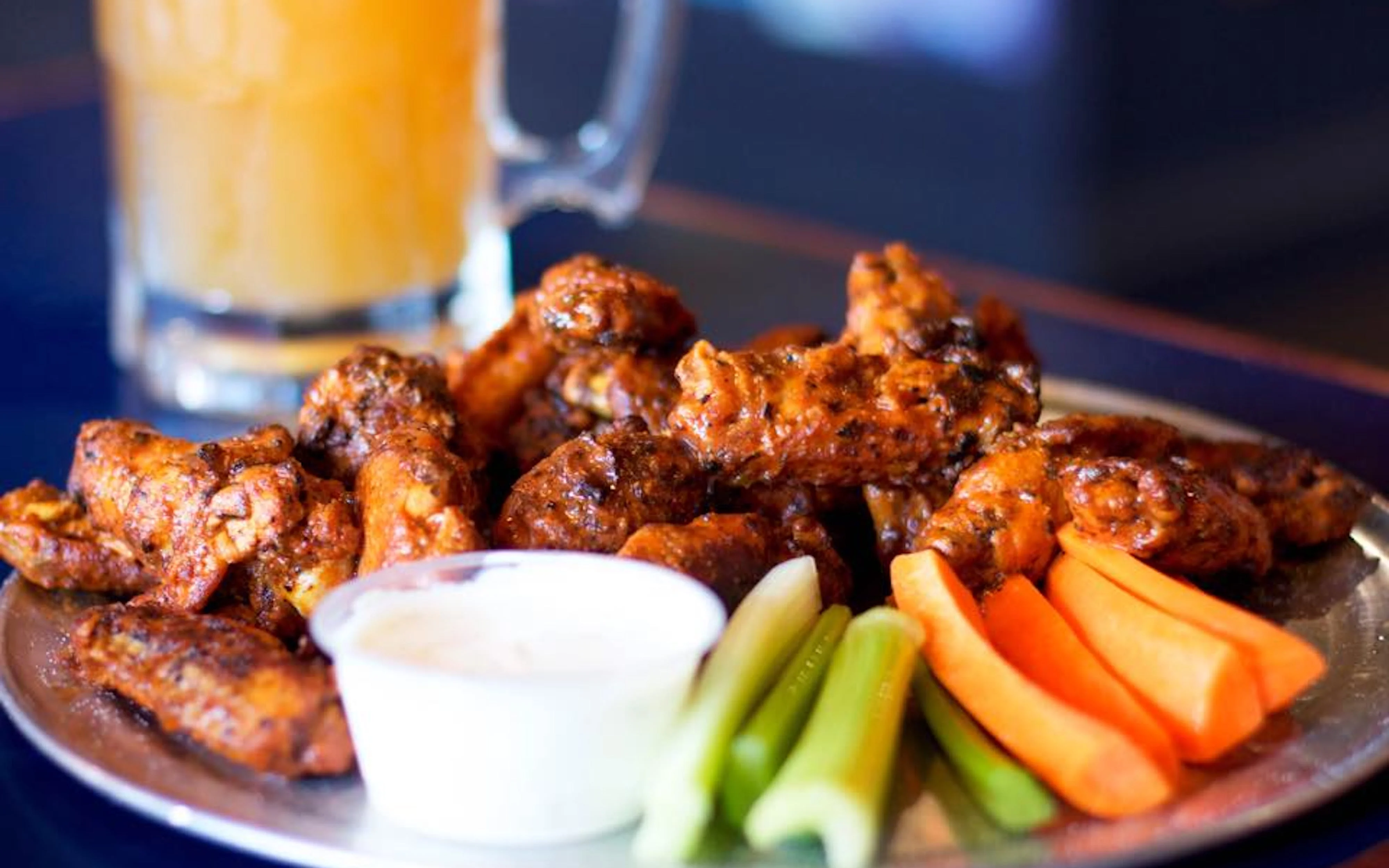 Plate of glazed chicken wings served with celery sticks, carrot sticks, and a side of dipping sauce.