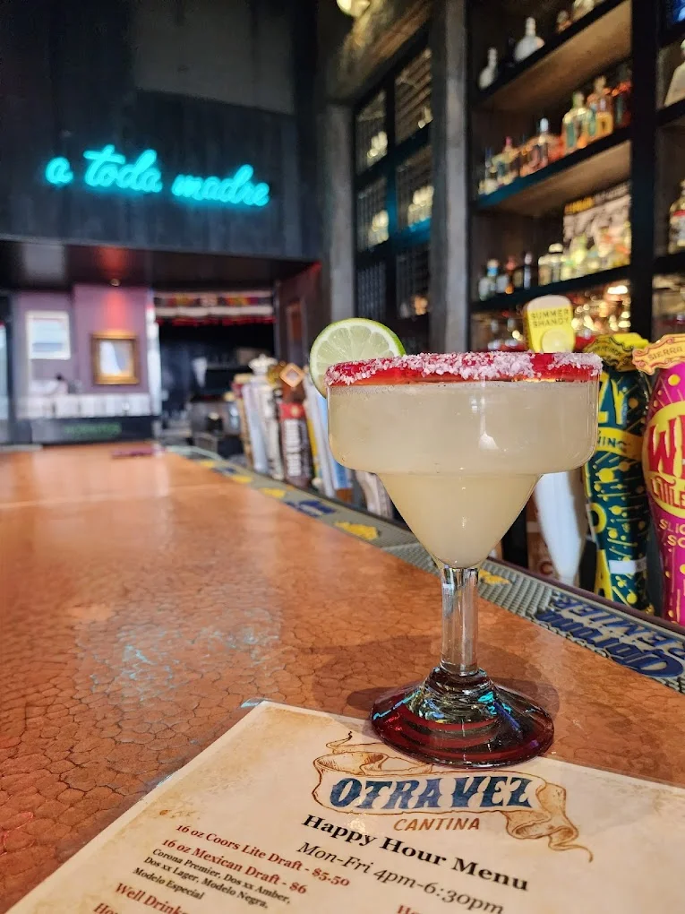 A margarita cocktail garnished with a lime wedge and a salted rim, placed on a bar top with a menu visible.