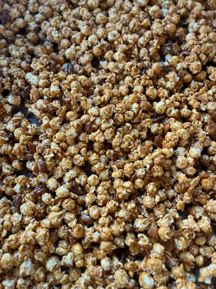 A close-up of popcorn coated in a crunchy caramel mixture, scattered evenly with some pecans mixed in.