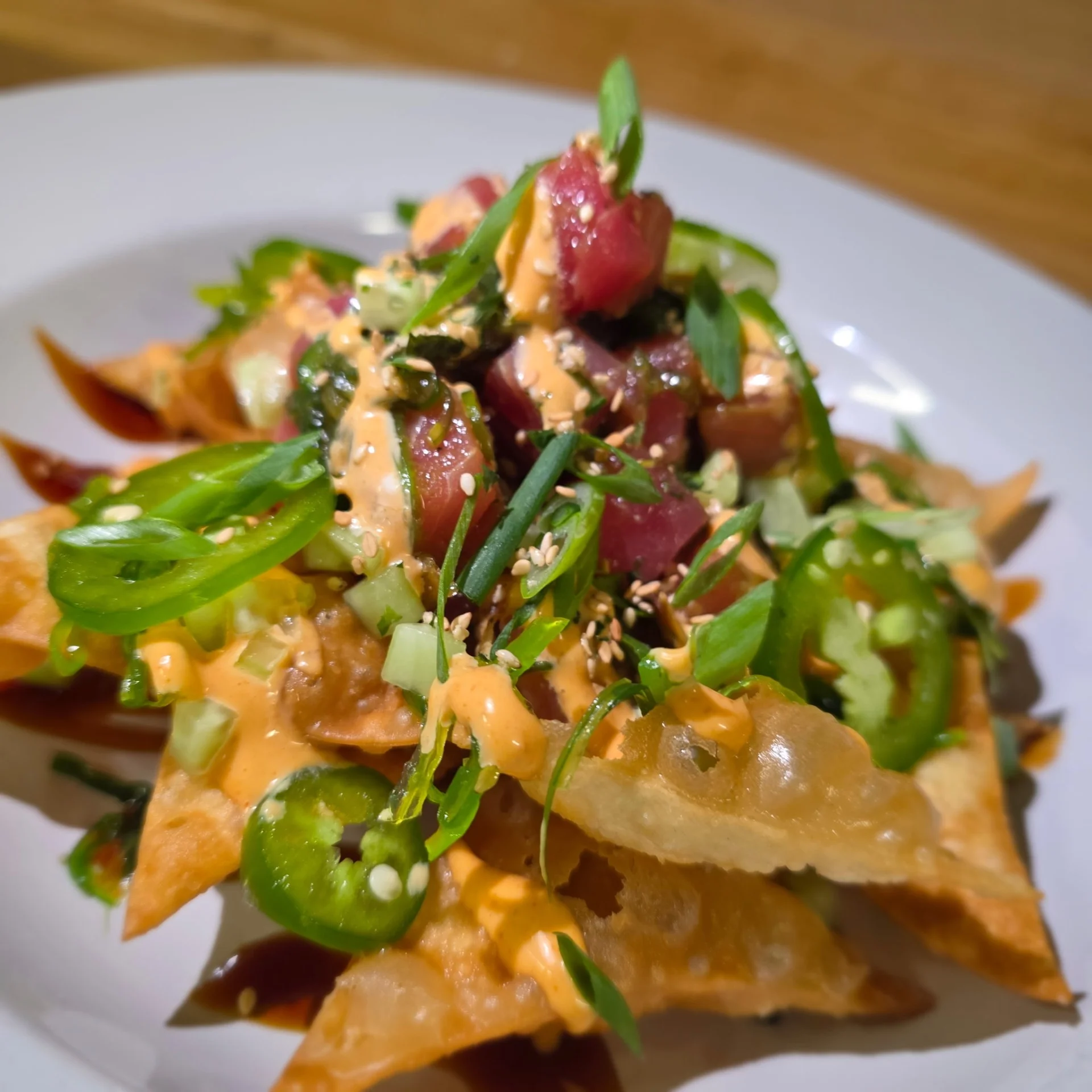 Plate of nachos topped with tuna, green onions, and spicy sauce.