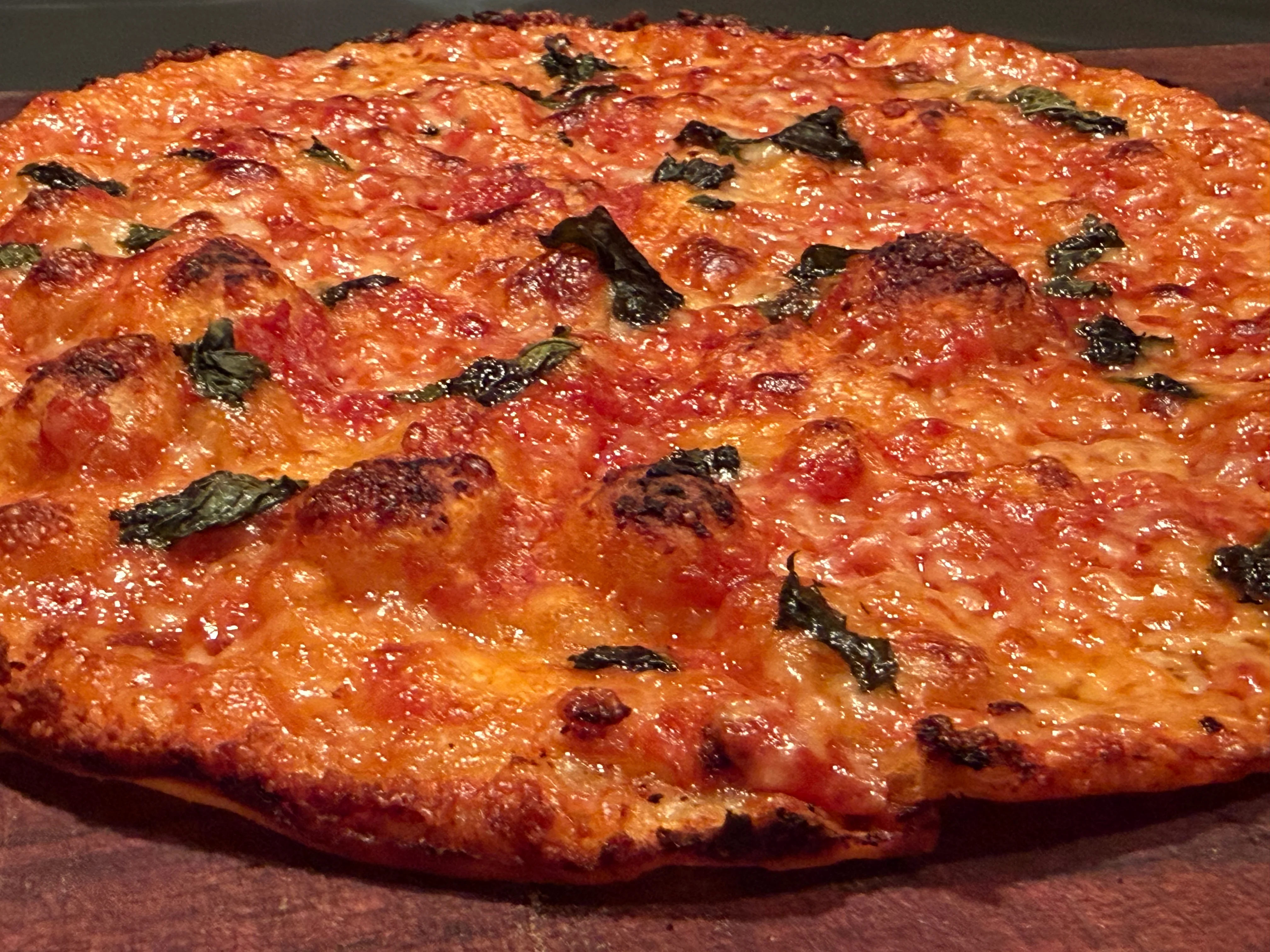A freshly baked pizza topped with melted cheese and fresh basil leaves. The crust is golden and slightly charred.