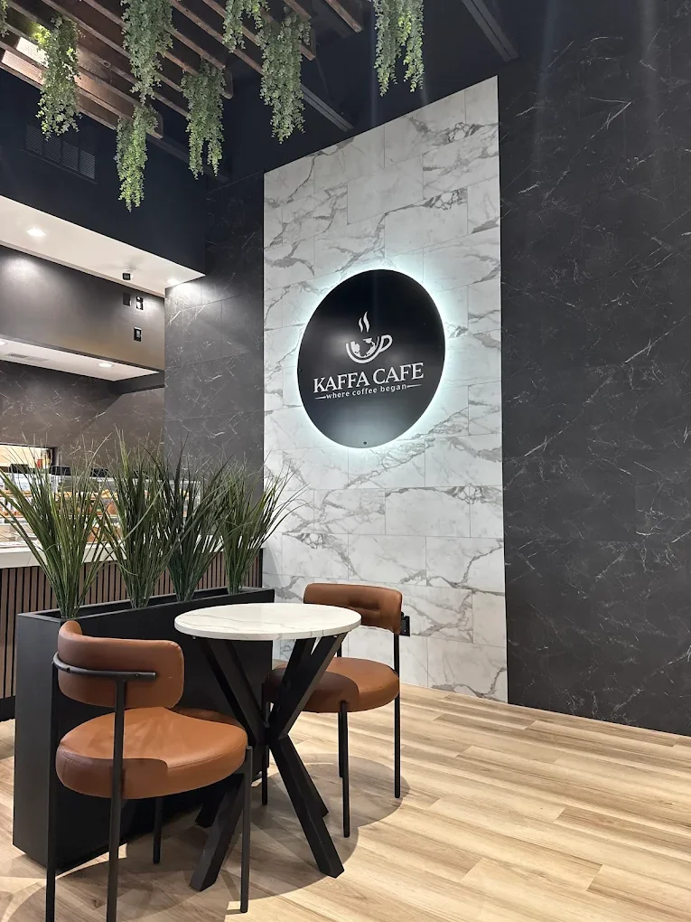 A cozy corner of a café featuring a round table and two brown chairs, with a decorative plant and stylish wall design as the backdrop.