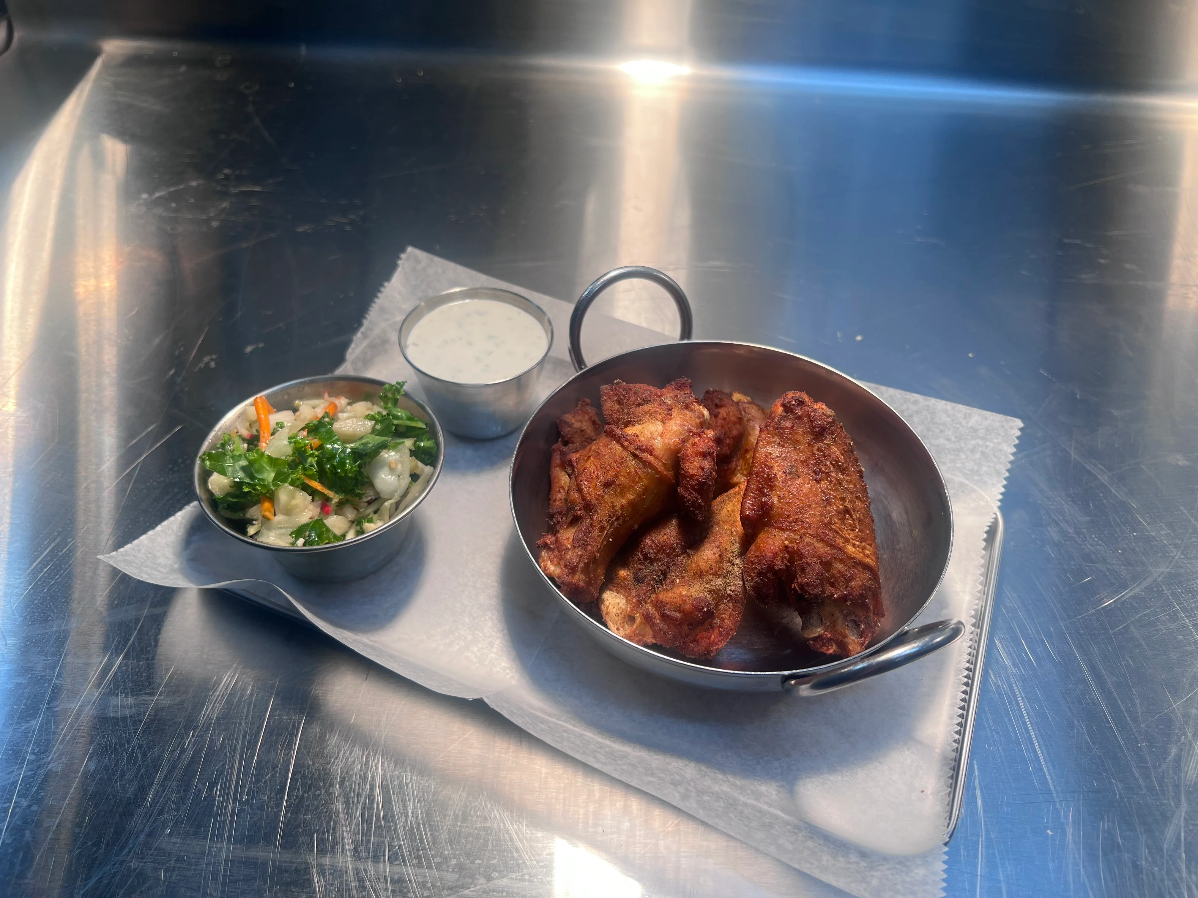 Fried chicken wings with salad and dipping sauce on a metal surface.