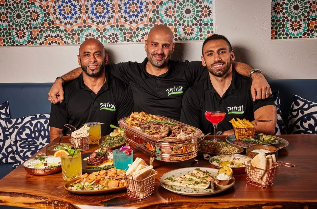 An inviting spread of Mediterranean dishes on a wooden table, featuring grilled meats, rice, pita bread, vibrant salads, and colorful drinks.