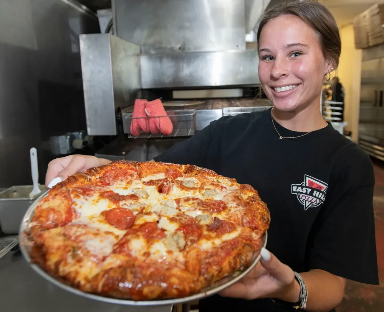 Smiling pizzeria worker presenting a freshly baked pepperoni pizza