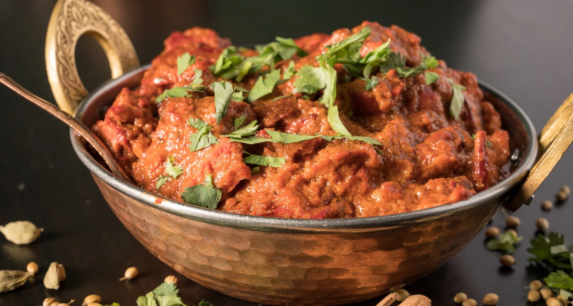 An artfully presented bowl of authentic Butter Chicken from Mint Indian Restaurant, served in a traditional hammered copper karahi and surrounded by whole spices.