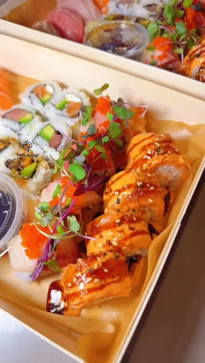 A close-up of a sushi roll topped with vegetables and sauce, presented on a white plate.