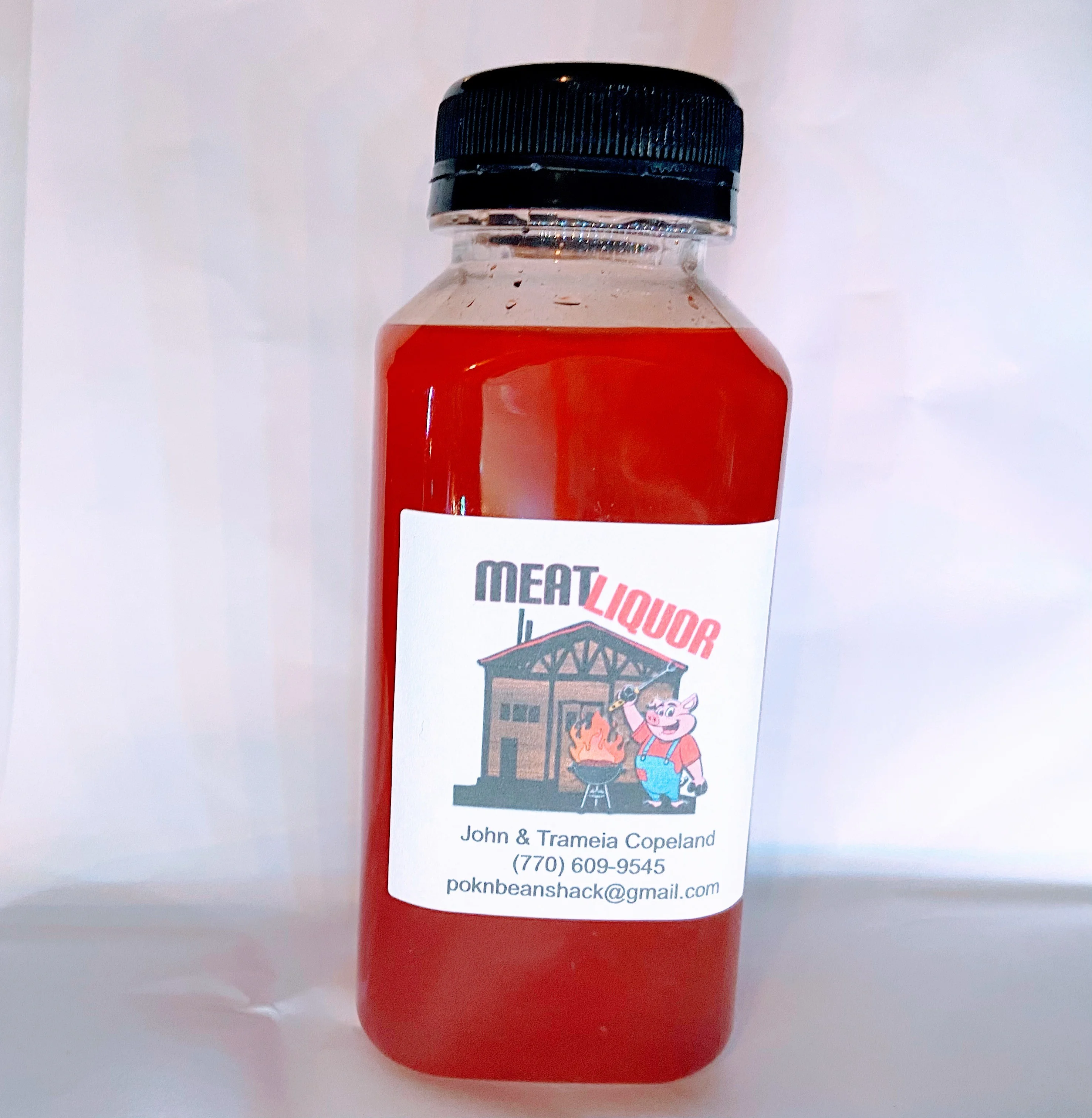 A bottle of red liquid labeled 'MEATLIQUOR'. The bottle has a black cap and a cartoonish illustration of a pig and a burning grill.