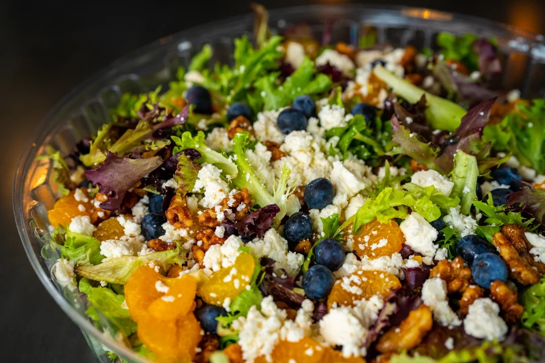 A fresh salad featuring mixed greens, blueberries, orange segments, and crumbled cheese, topped with walnuts.