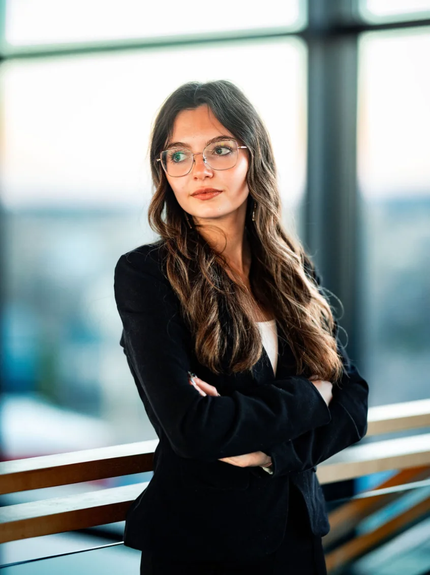 Professional woman in a black suit with glasses, standing confidently indoors