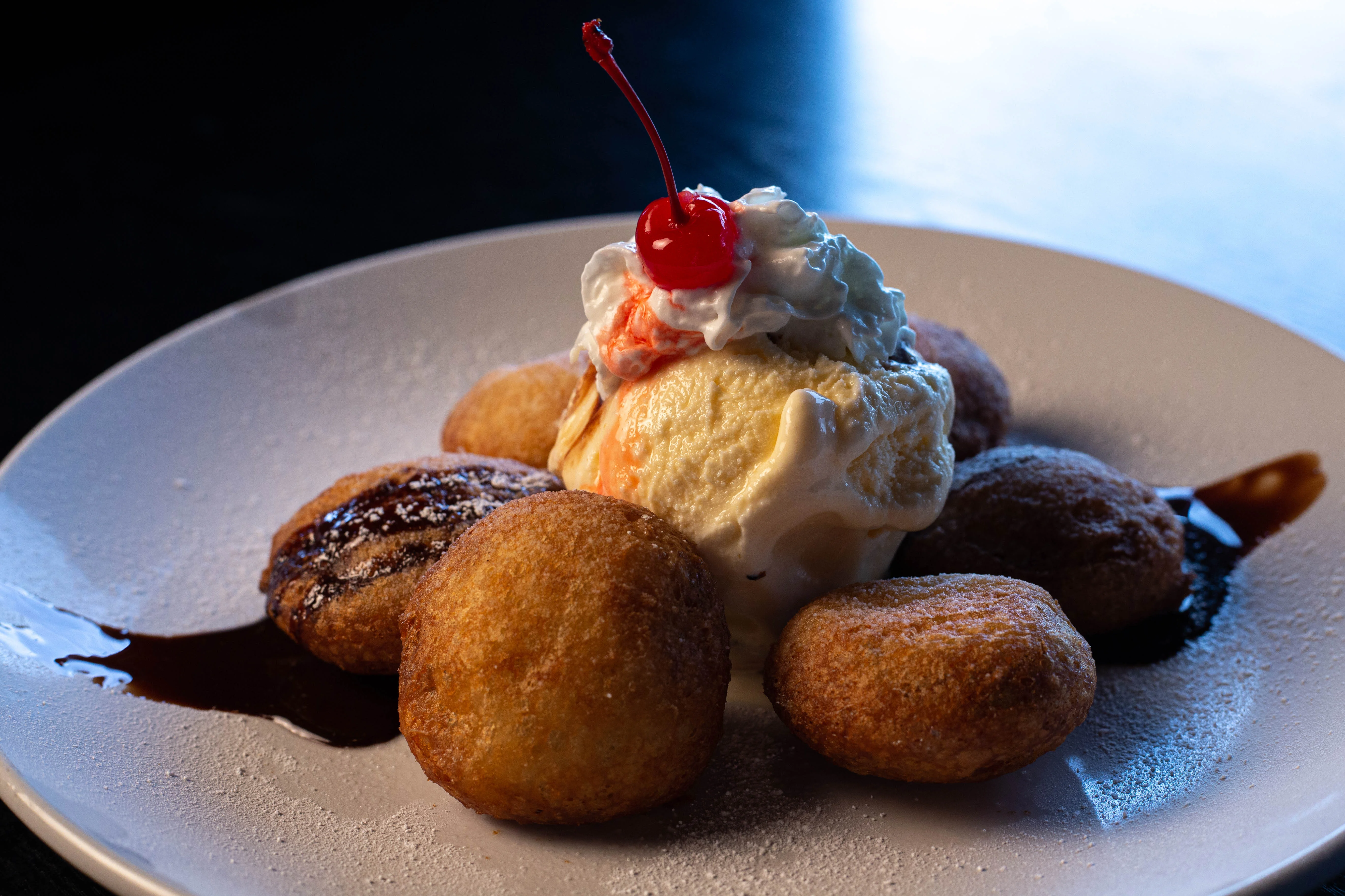 A plate of deep-fried pastries arranged around a scoop of vanilla ice cream with whipped cream and a cherry on top.