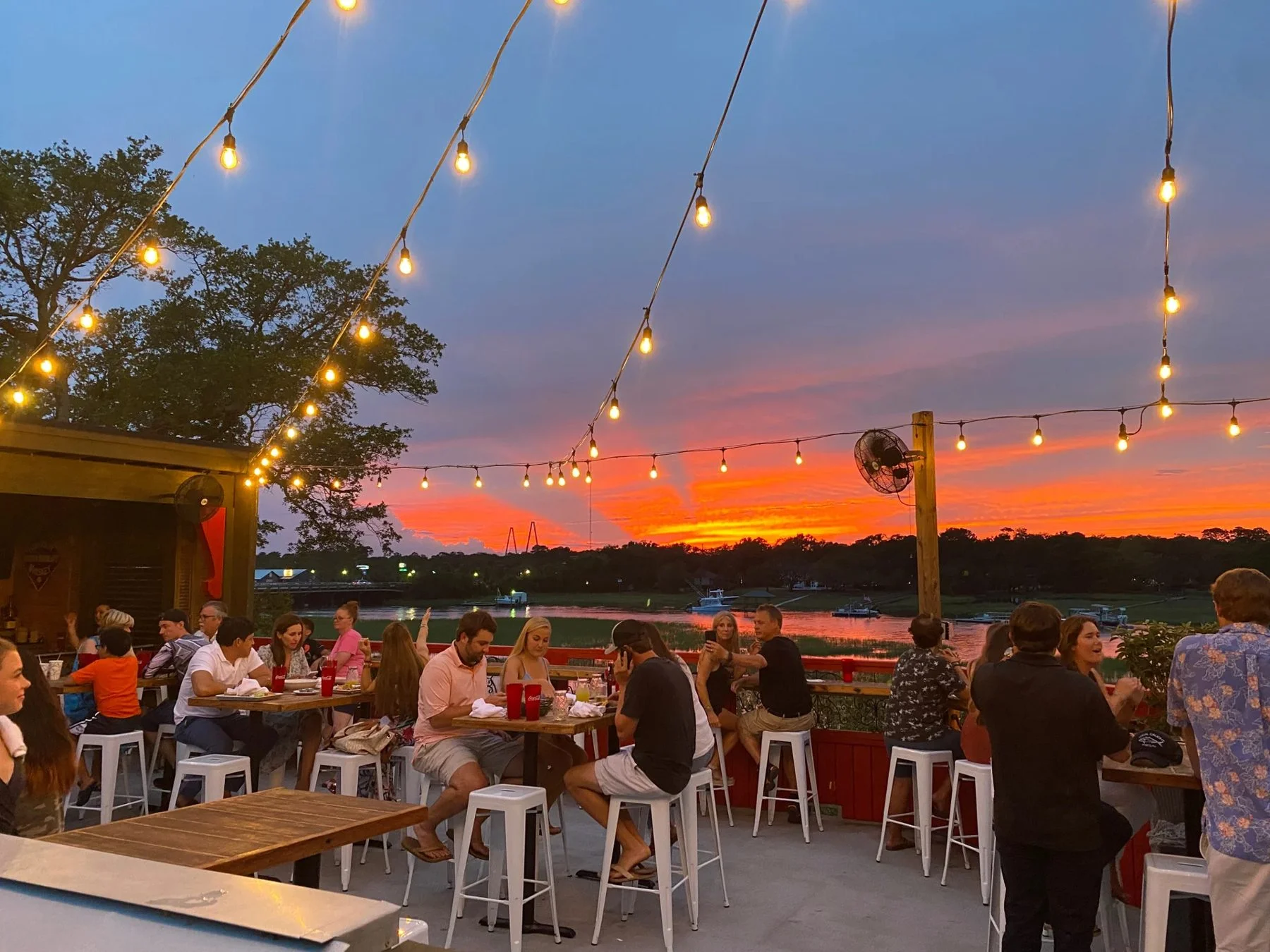 Outdoor restaurant patio overlooking a river at sunset with string lights
