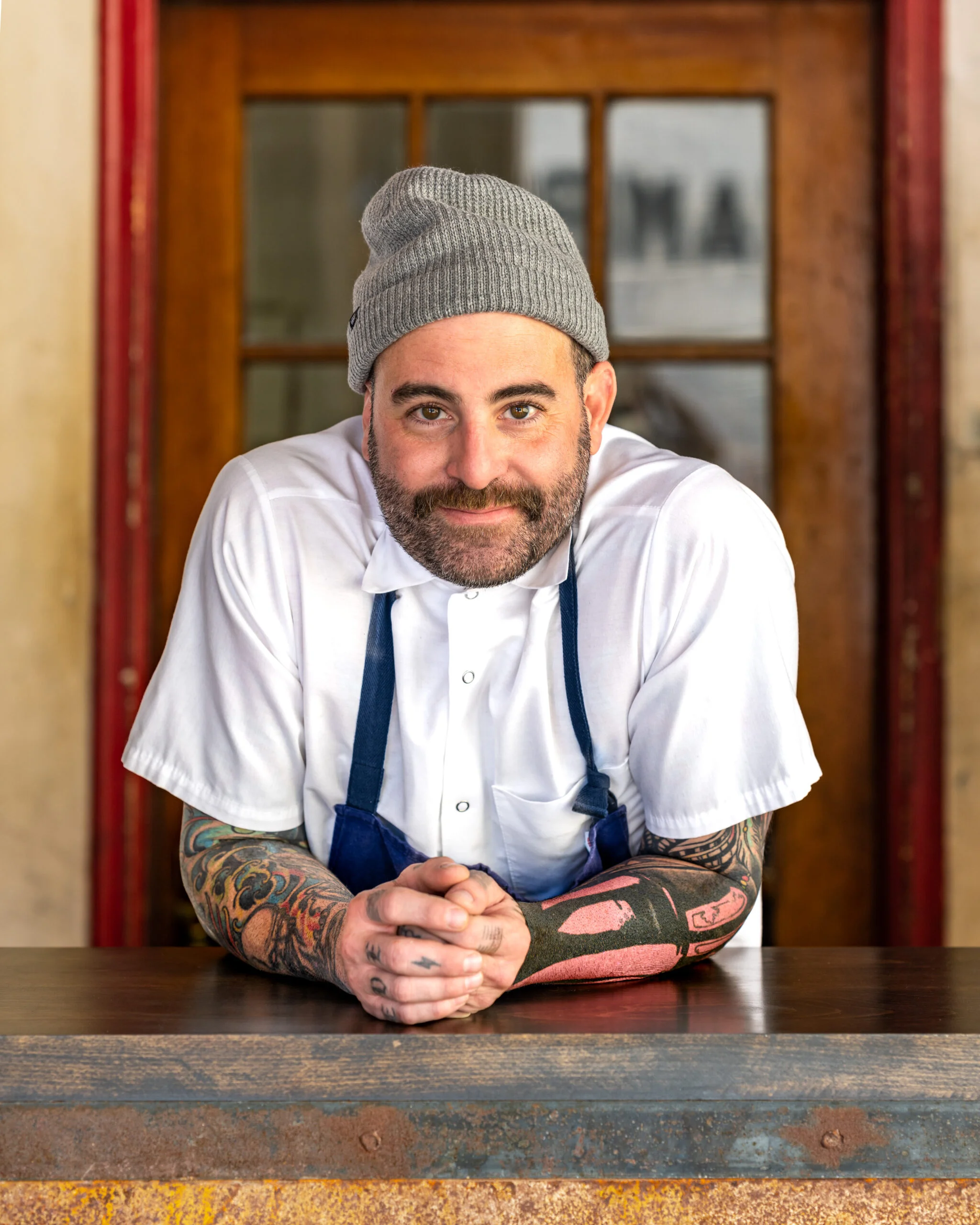 Chef with tattoos and beanie at restaurant counter