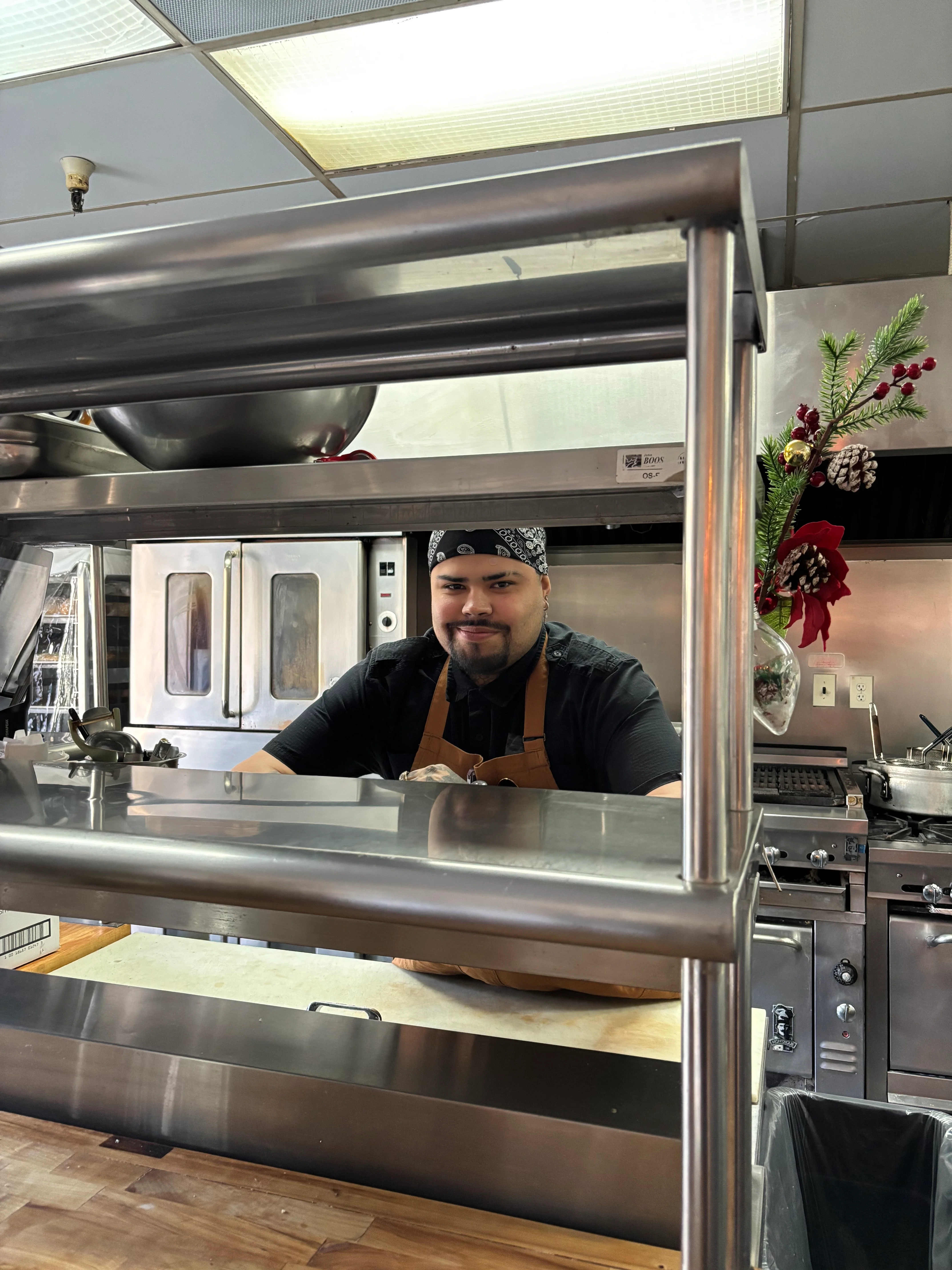 Chef in a kitchen smiling behind a stainless steel counter.