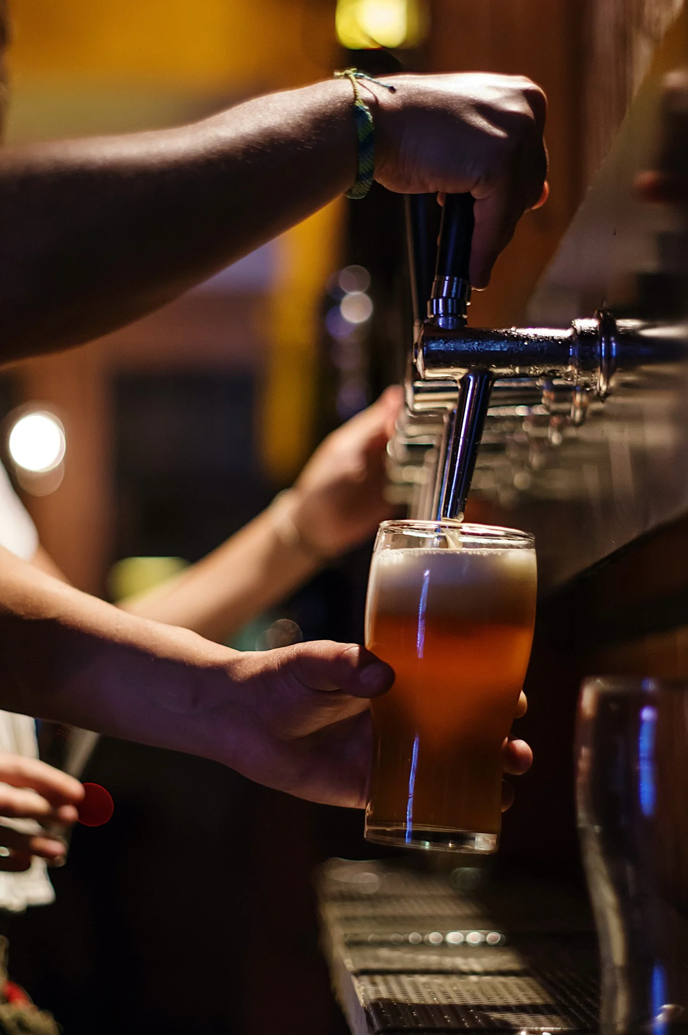 A hand pouring beer into a glass from a tap, with the background softly blurred to focus on the pouring action.