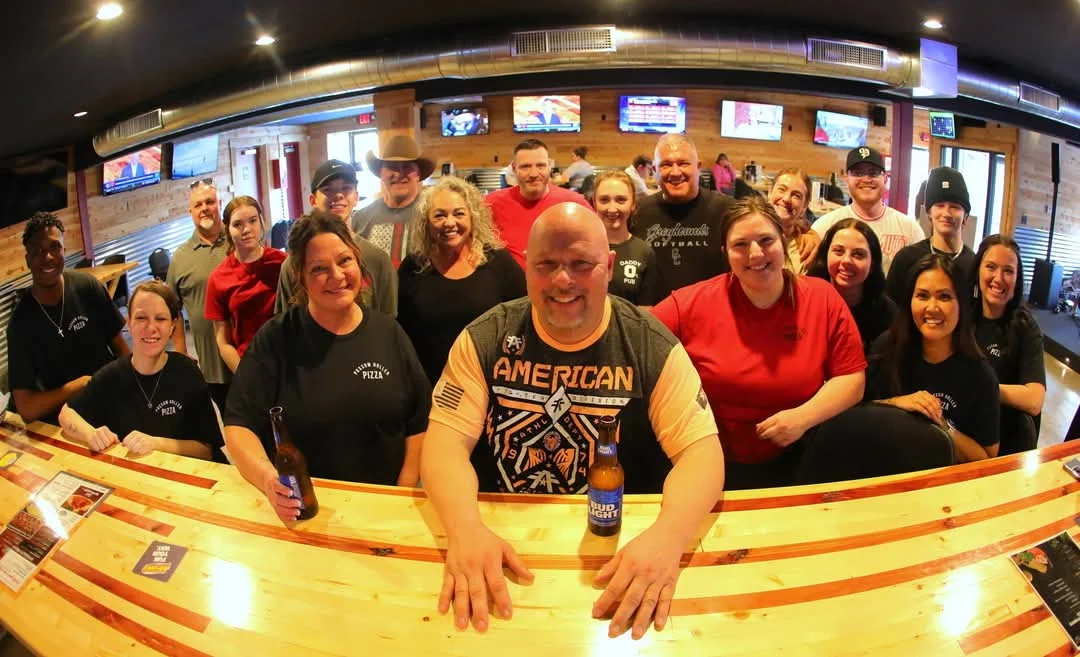 Group photo of restaurant staff and patrons at a bar with drinks.