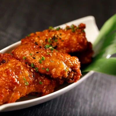 A plate of glazed chicken wings topped with green onions, presented in a white dish.