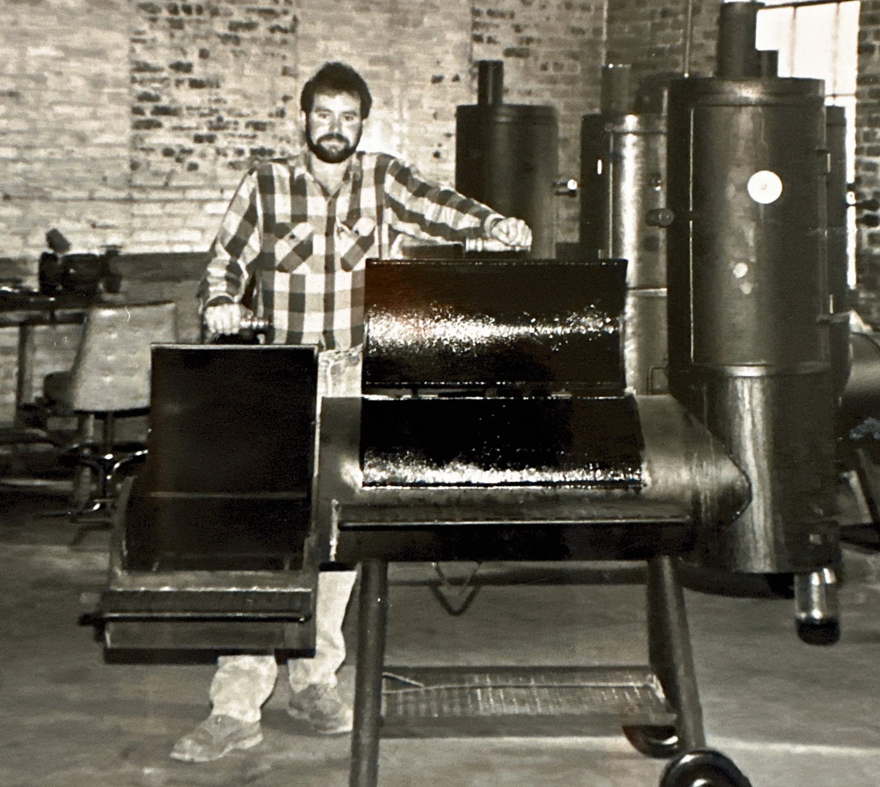 Man posing with a large barbecue smoker in a rustic workshop