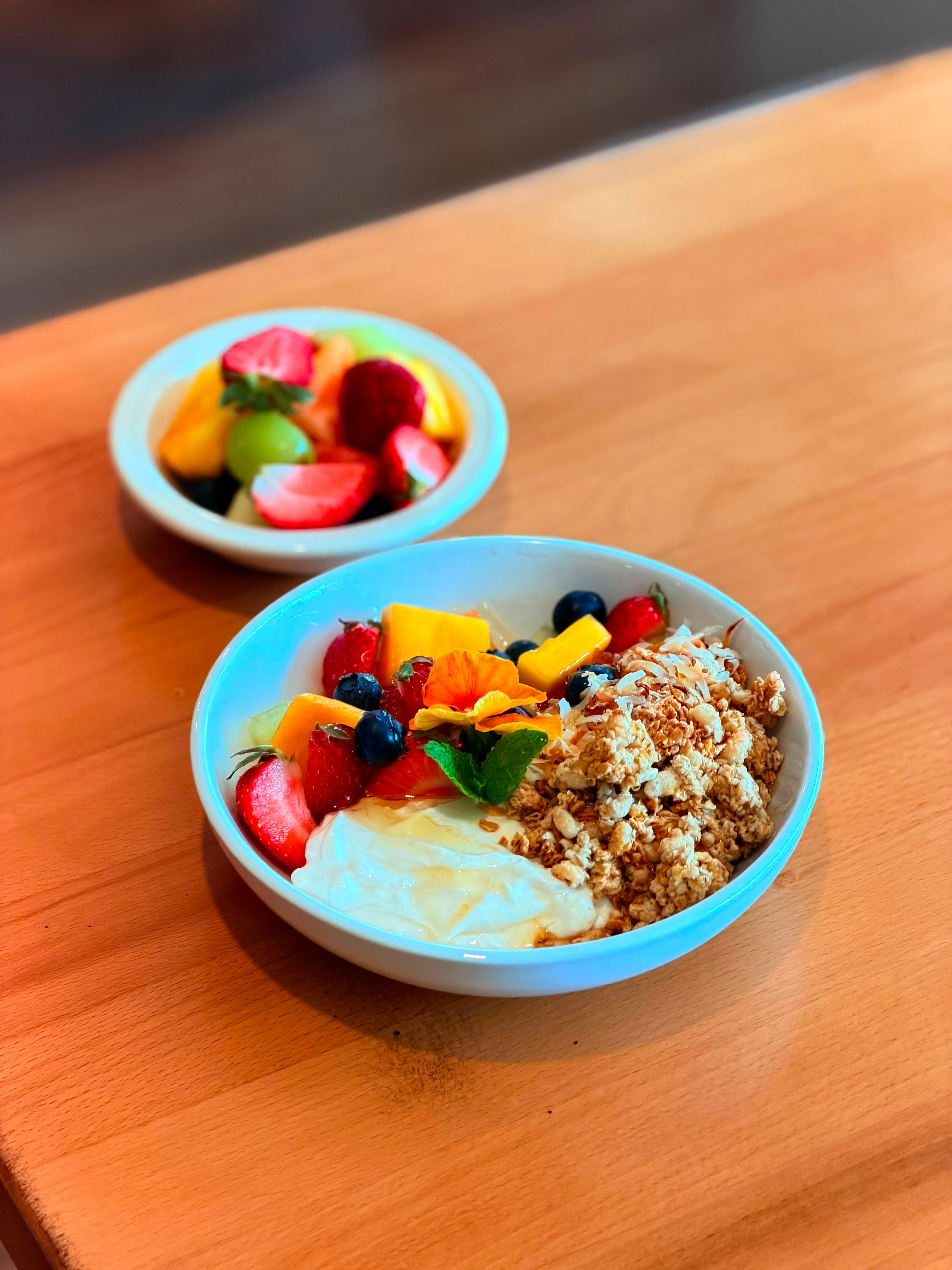 A bowl of yogurt topped with granola and an array of fresh fruits, alongside a small bowl of mixed fruit.