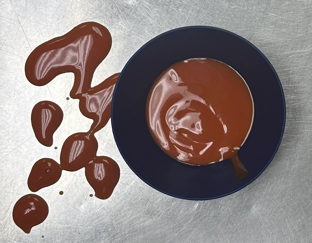 Rich chocolate sauce in a bowl with drizzles on a metallic surface