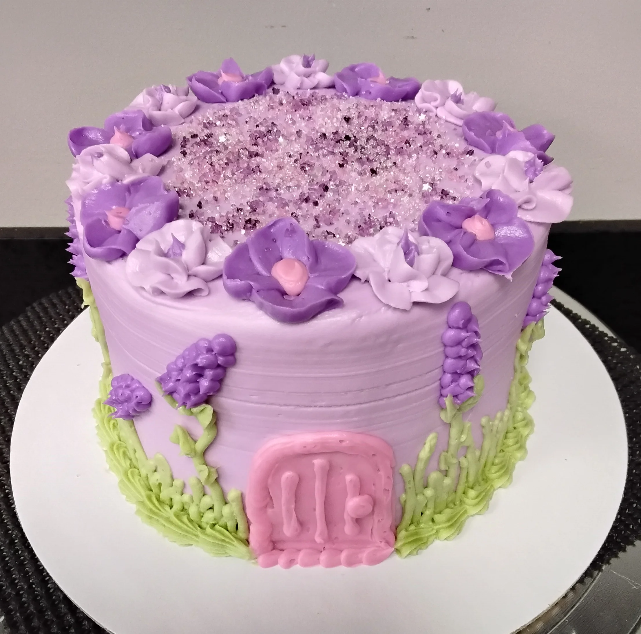 Whimsical fairy door cake with flowers, mostly purple with pops of green & pink.