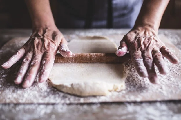 Baker rolling dough on a floured surface