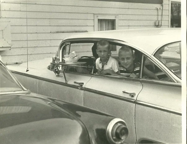 Two children smiling from a classic car window