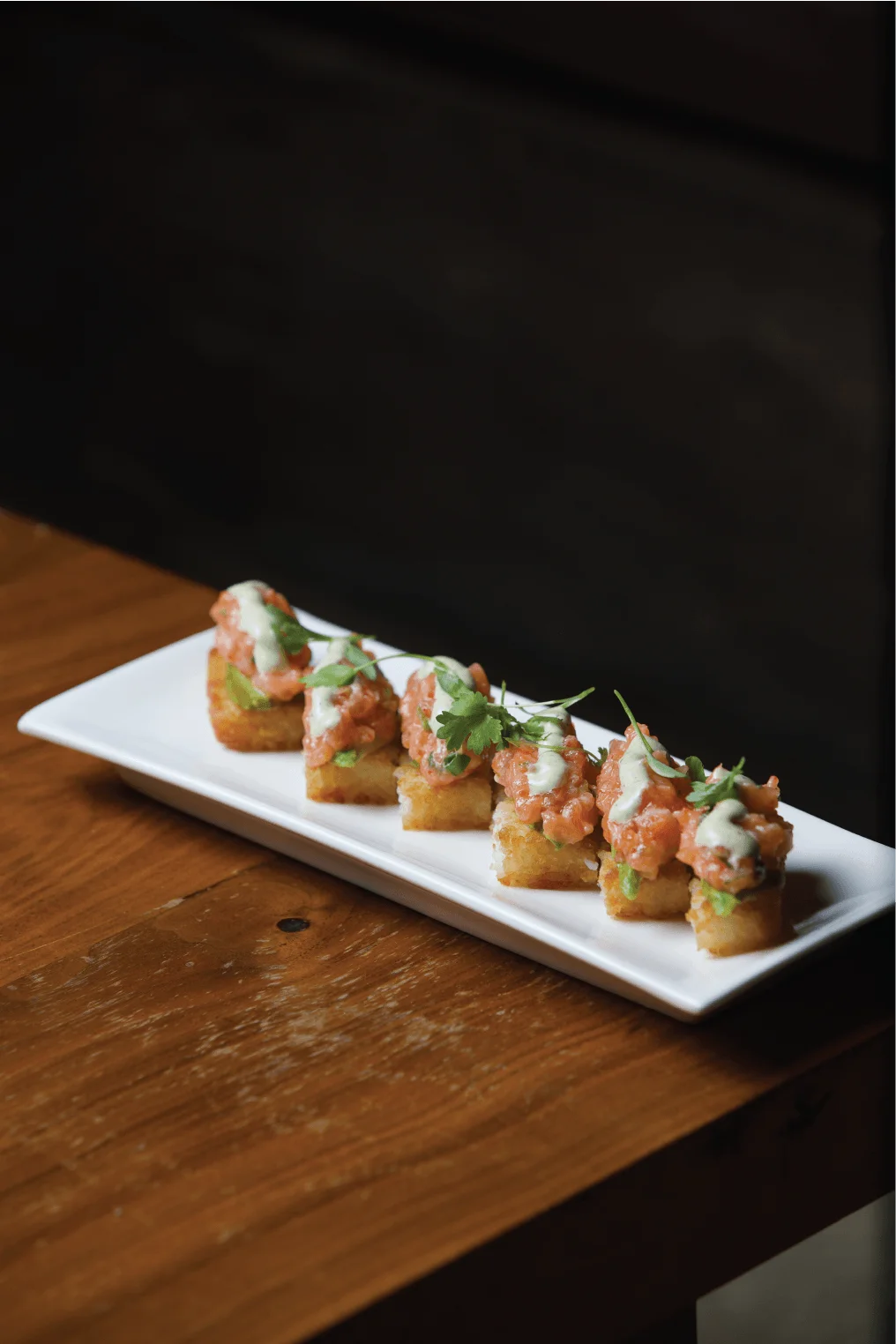 Five pan-seared pork or vegetable dumplings garnished with microgreens, served on a white rectangular plate with a side of dipping sauce.