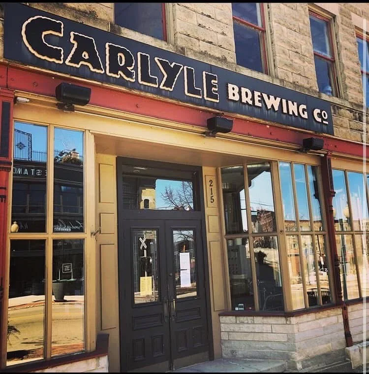 The exterior of a brewery featuring large glass windows and a decorative sign.