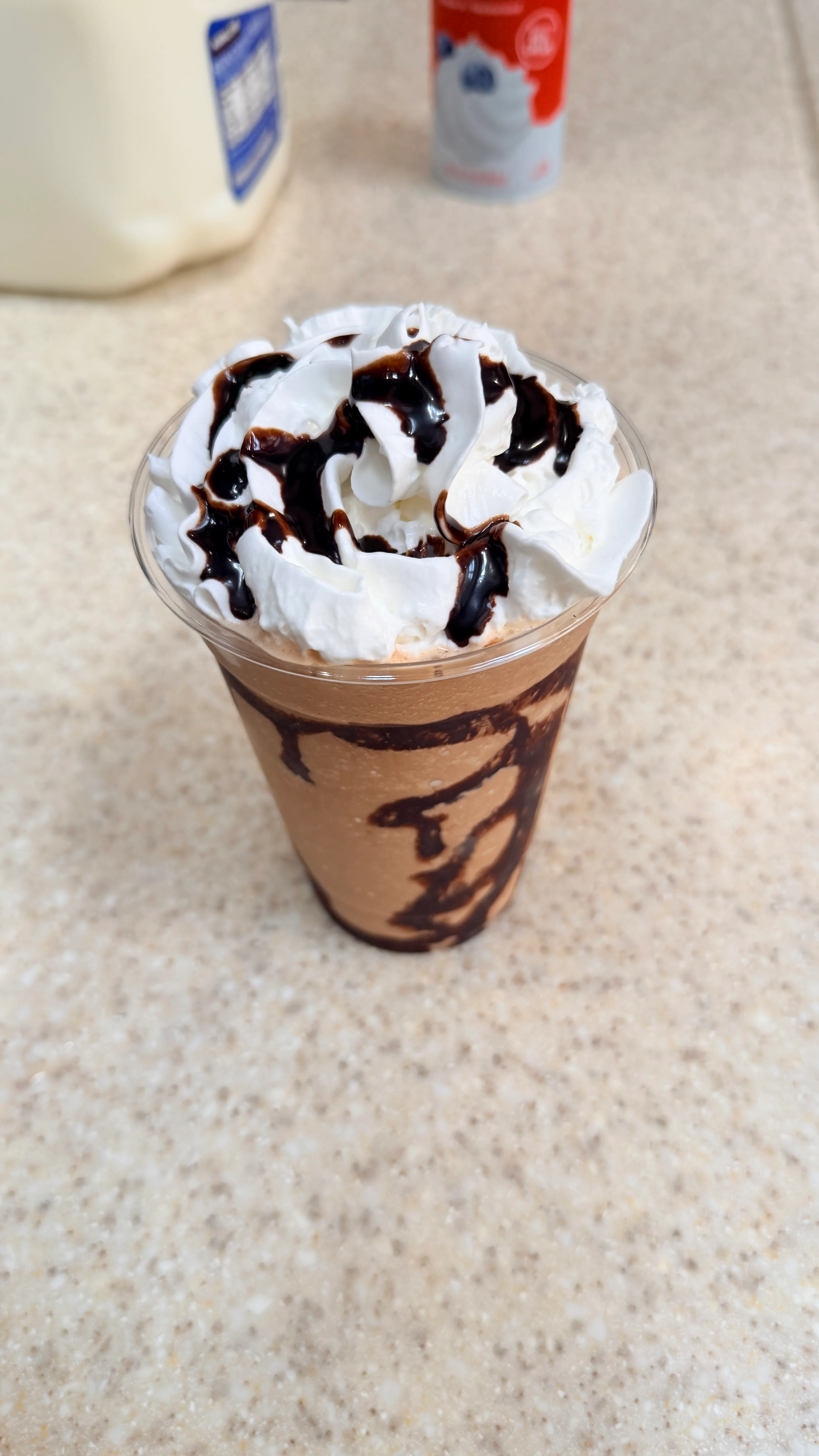 Chocolate milkshake topped with whipped cream and chocolate drizzle.