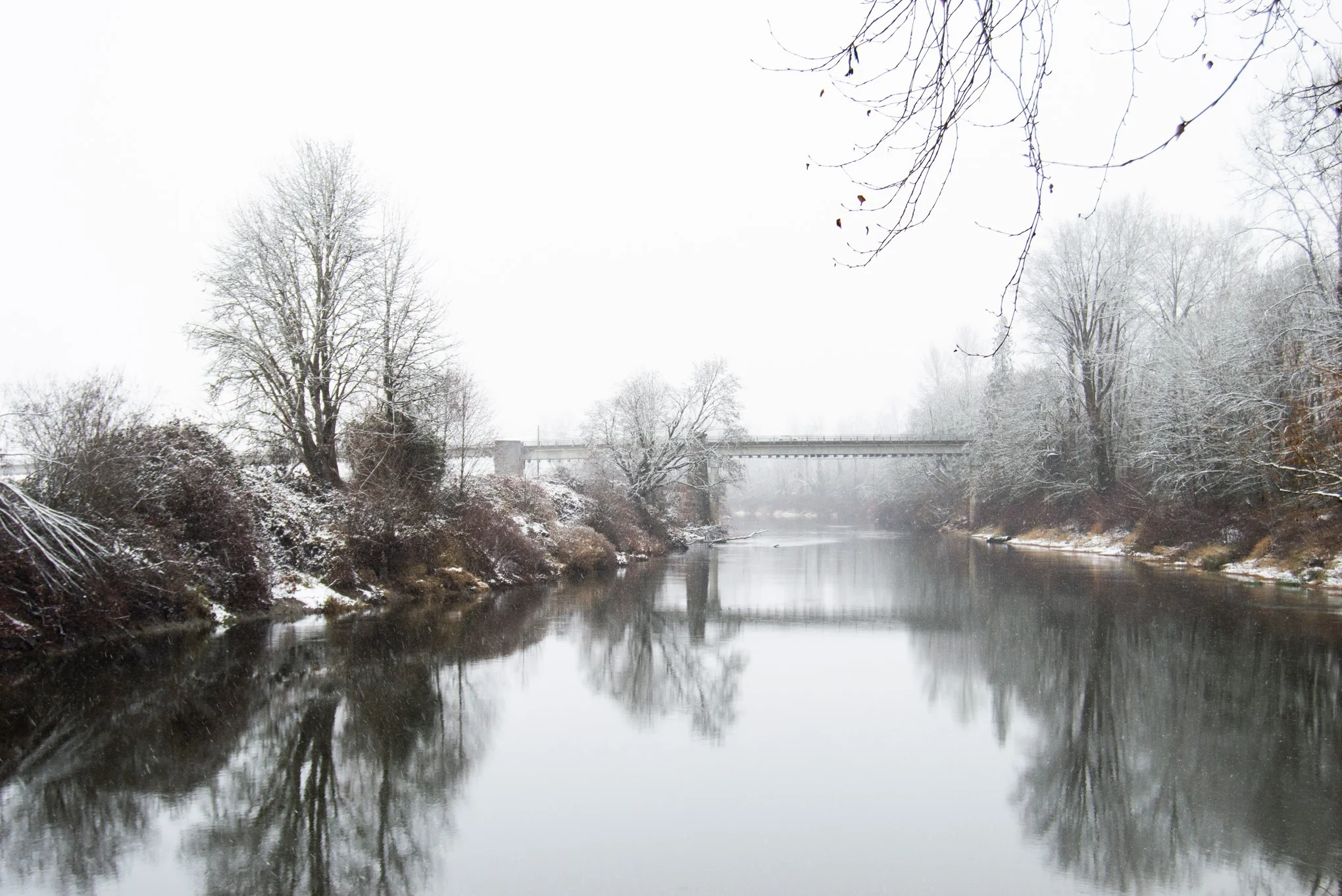 Snowy river landscape with a bridge and trees in winter