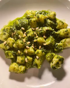 A serving of gnocchi topped with pesto sauce, garnished with pine nuts. The dish is presented on a white plate, showcasing vibrant green colors.