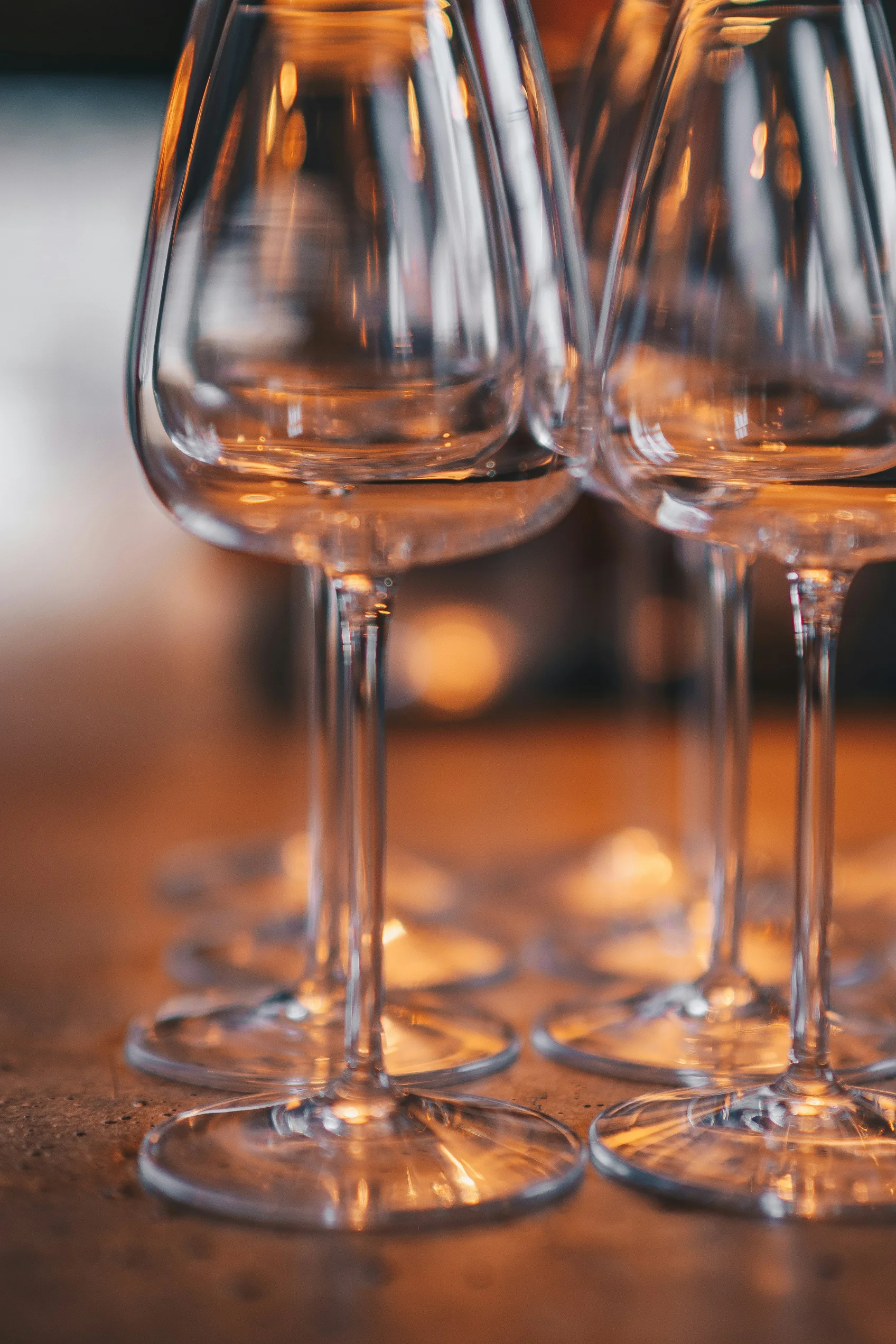 A collection of elegant wine glasses arranged on a bar surface, reflecting warm lights from above.