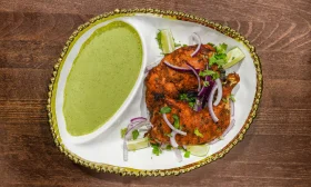 A serving of grilled chicken pieces with a green sauce, garnished with onions and fresh herbs on a decorative plate.