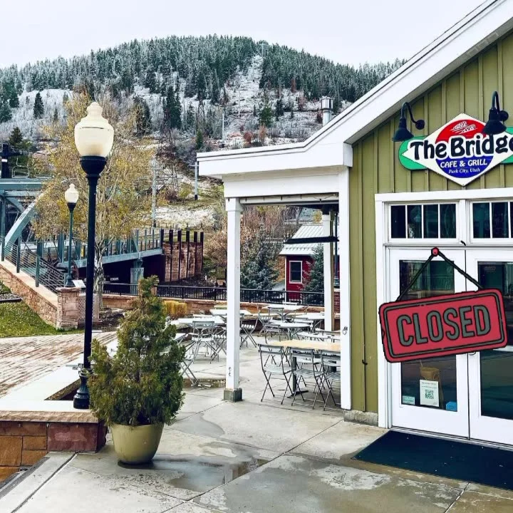 A cafe with a 'CLOSED' sign, set against a backdrop of a mountain and a snowy landscape. Tables are arranged outside, hinting at a cozy dining space.