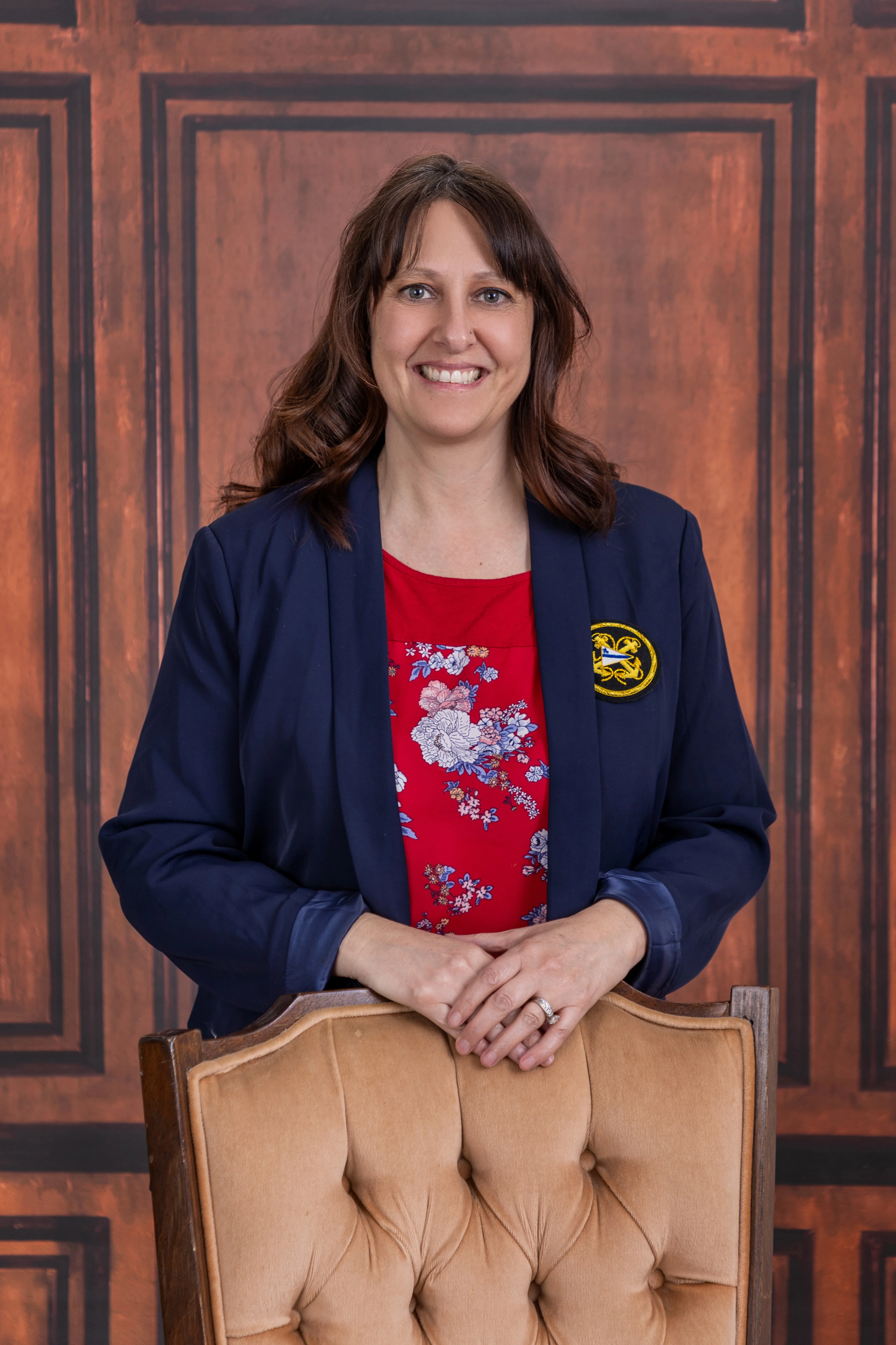 Professional woman smiling in a navy blazer against a wooden backdrop