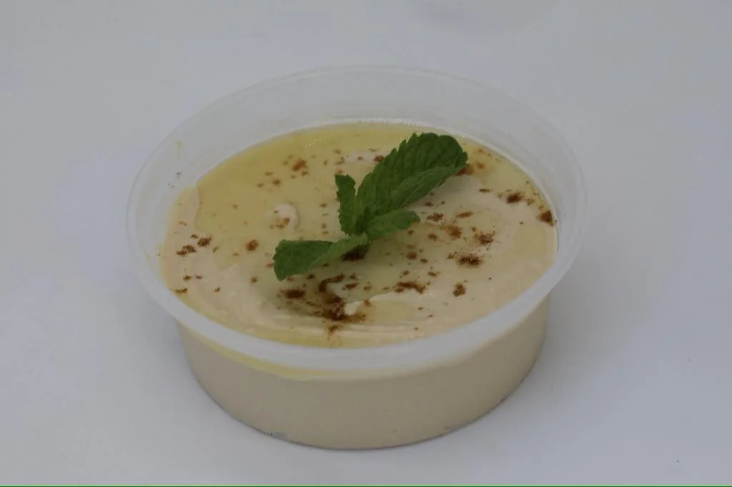 A small clear cup containing a creamy dessert, topped with a mint leaf and a sprinkle of cinnamon.